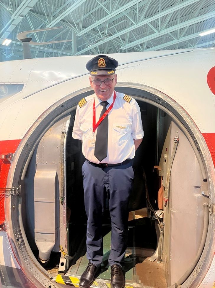 A man in a pilot's uniform standing in the doorway of an air canada model plane